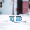 Two blue mugs with cartoon character on a snowy surface