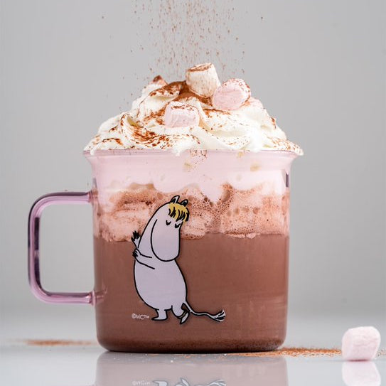 Hot chocolate with whipped cream and marshmallows in a glass mug with a cartoon character handle.