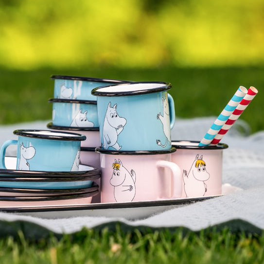Set of enamel mugs with cartoon characters on a grassy background