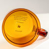 Amber-colored mug with a quote and brand name on a white background