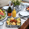 Dining table set with appetizers, drinks, and flowers on a white tablecloth.