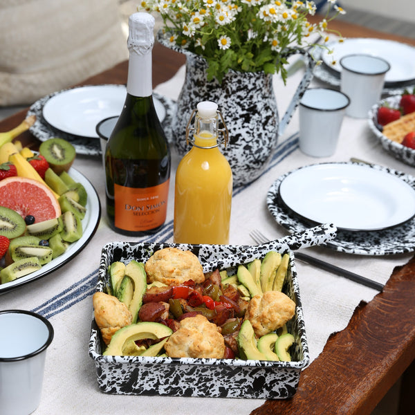 Dining table set with appetizers, drinks, and flowers on a white tablecloth.