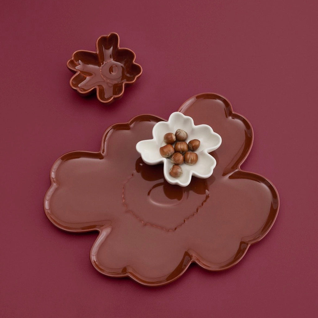A flower-shaped brown ceramic serving platter with a matching small flower-shaped dish, shown on a dark burgundy background. A small white flower dish in the center holds brown nuts.