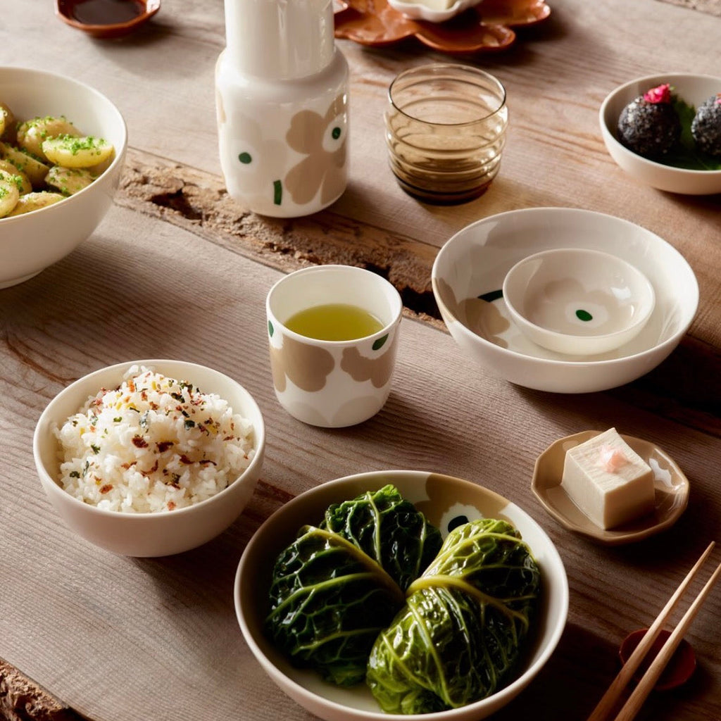 A styled Japanese dining table setting featuring a ceramic tableware set with a floral pattern, including bowls, a cup, a small pitcher, and a teapot, arranged with food on a rustic wooden table.