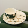 Ceramic cup and saucer with floral design on a green surface