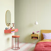 Modern bedroom with pink vanity, stool, and bed against a light green wall.
