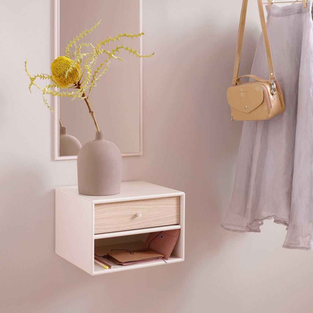 Small white wall-mounted shelf with a drawer, mirror, and decorative items in a minimalistic room.