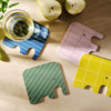 Four colorful elephant-shaped coasters on a wooden surface with a glass of tea and apples.