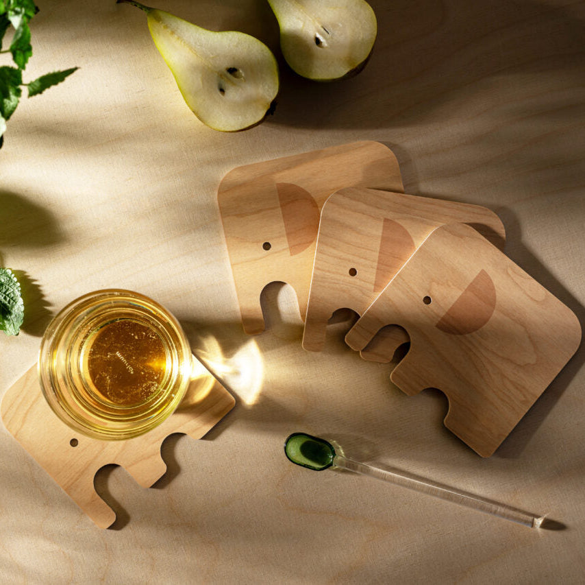 Wooden elephant coasters with a glass of yellow liquid on a wooden surface.