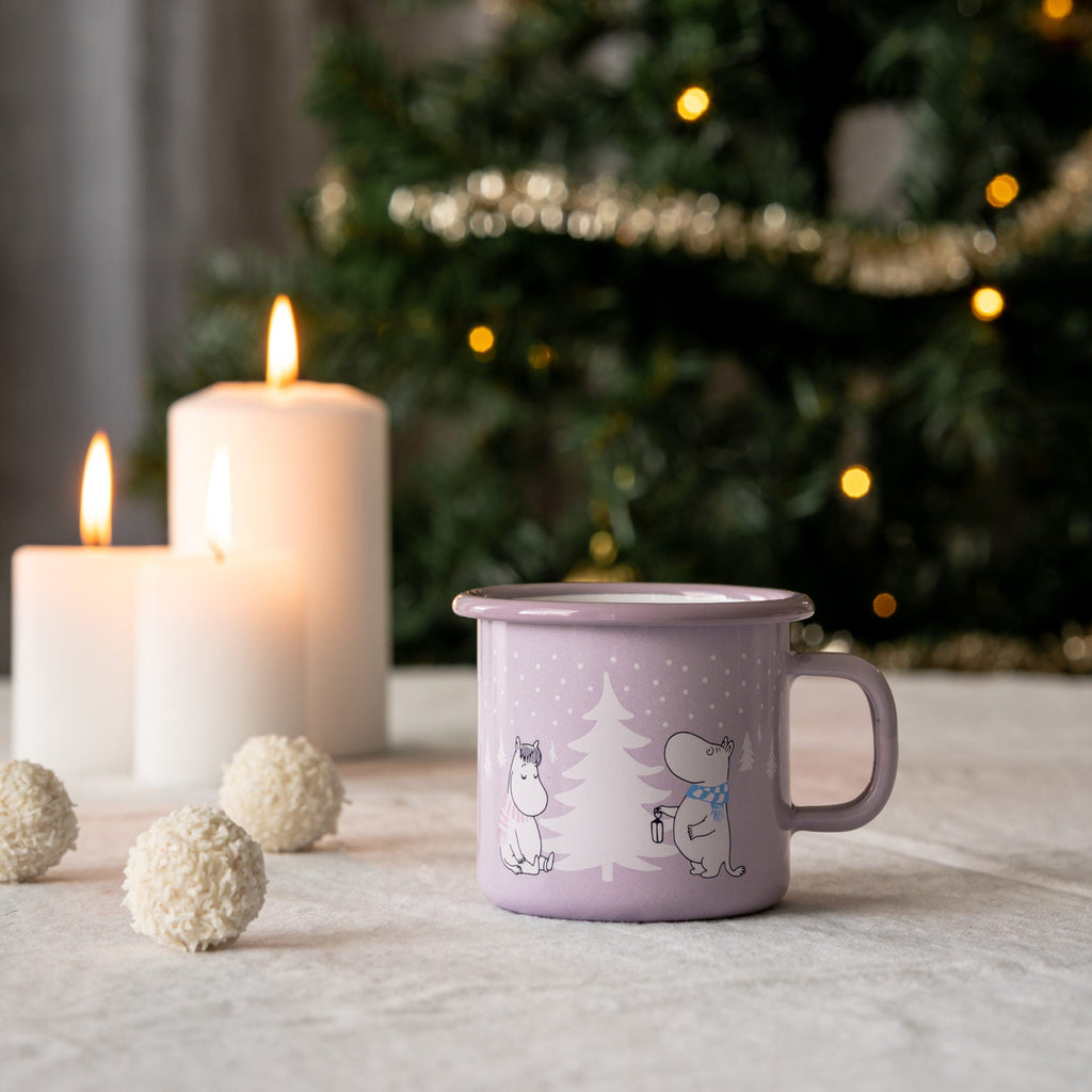 Purple mug with illustrations on a table with candles and a decorated Christmas tree in the background.