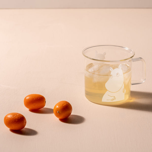 Clear glass mug with a handle on a beige surface, containing a liquid with a white animal illustration.