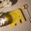 Yellow elephant coaster on a beige surface with a glass and pears