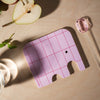 Pink elephant-shaped coaster on a beige surface with a glass and pears.