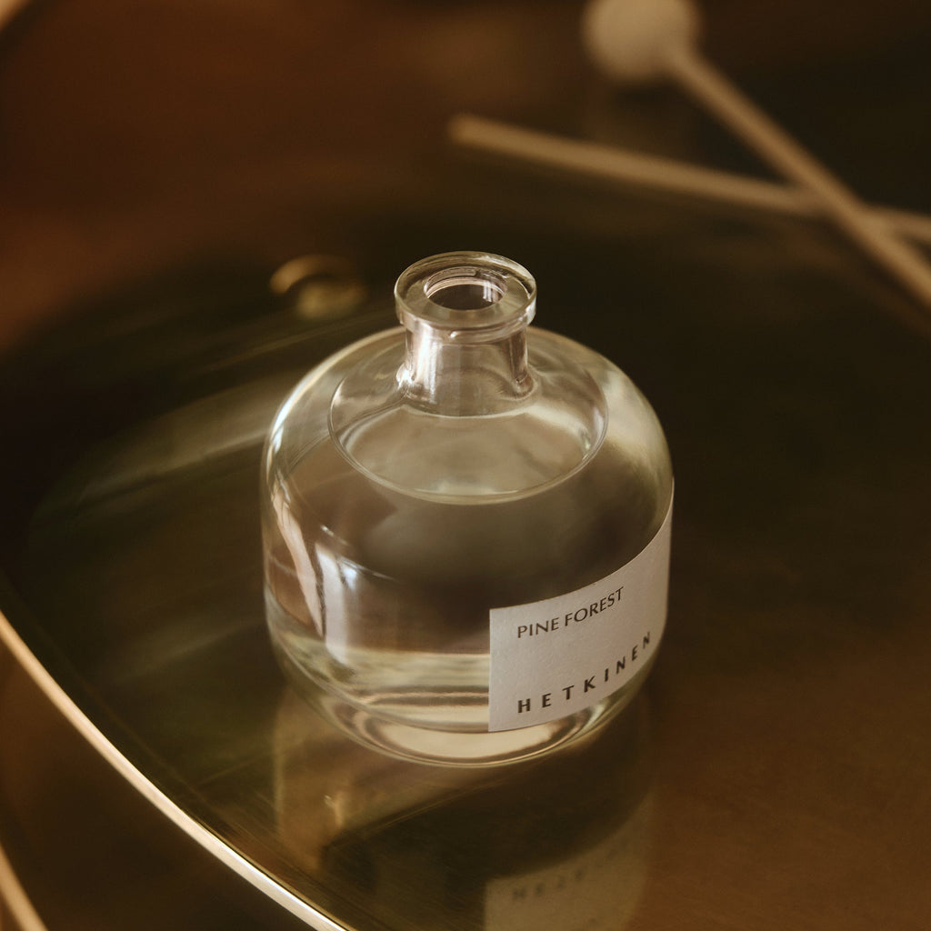 Clear glass bottle labeled 'Pine Forest' on a reflective surface with a blurred background