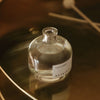 Clear glass bottle labeled 'Pine Forest' on a reflective surface with a blurred background